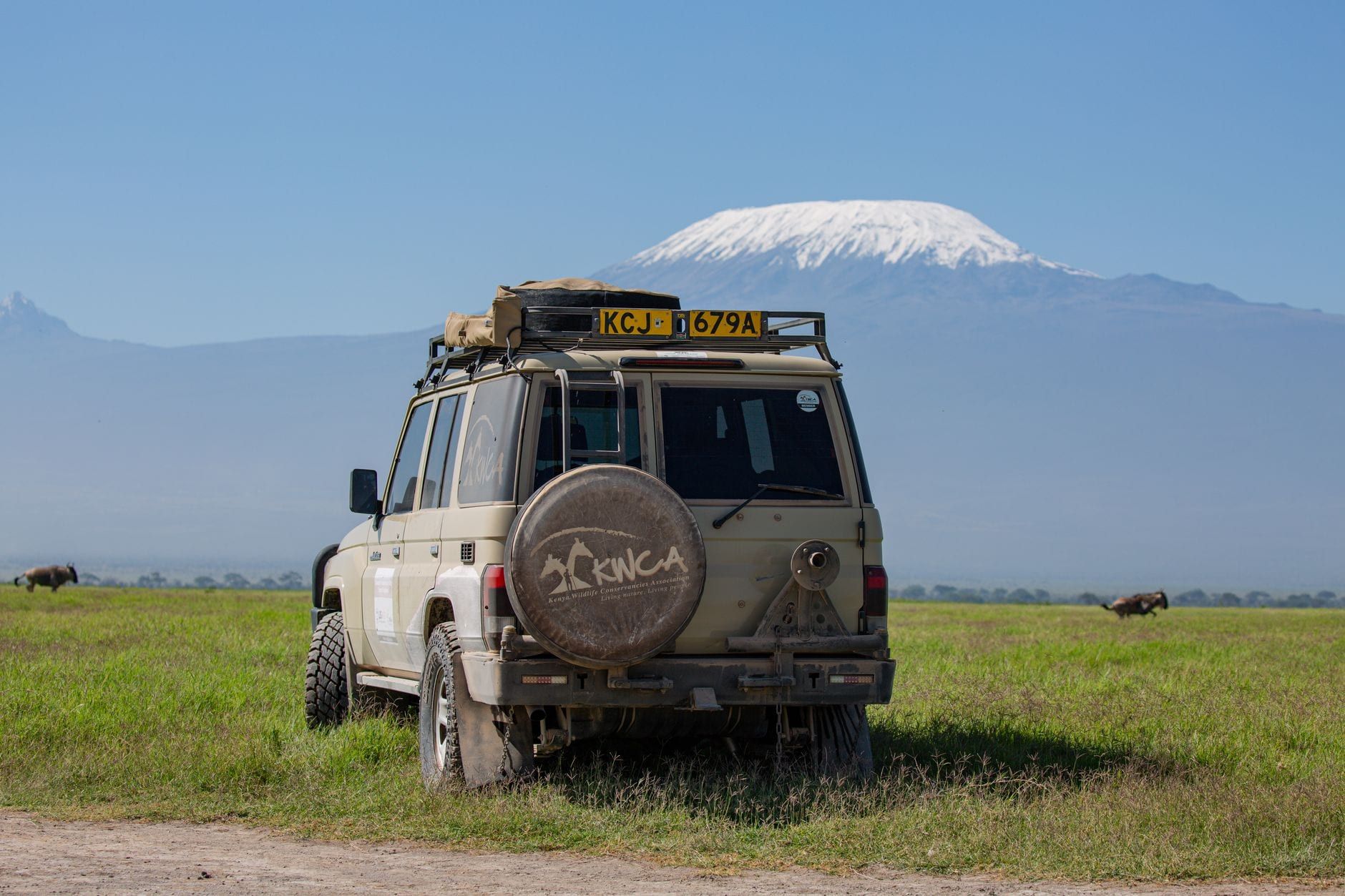Een safari-voertuig geparkeerd op de vlaktes van het Amboseli National Park met de sneeuwbedekte top van de Mount Kilimanjaro op de achtergrond.